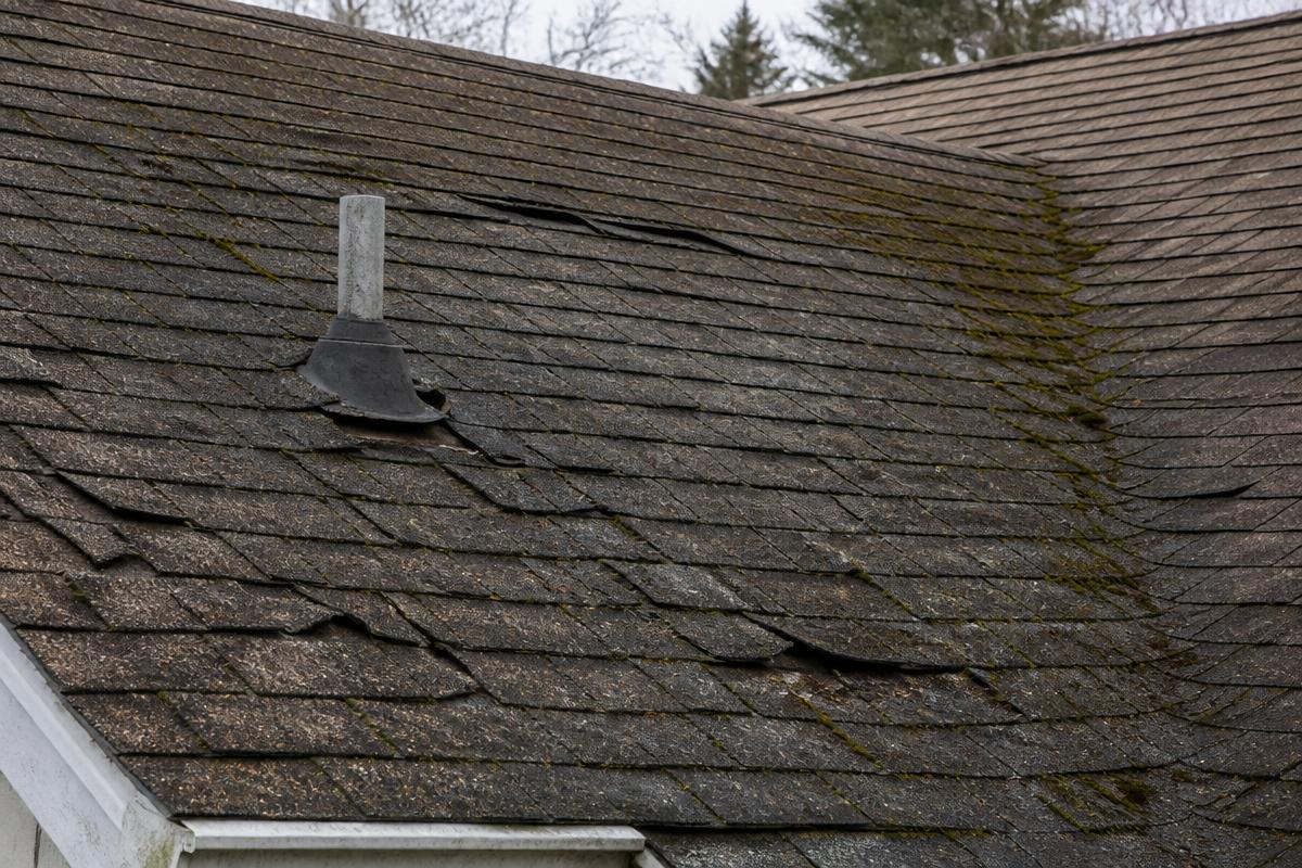 Worn Maine roof with moss growth and missing shingles before replacement
